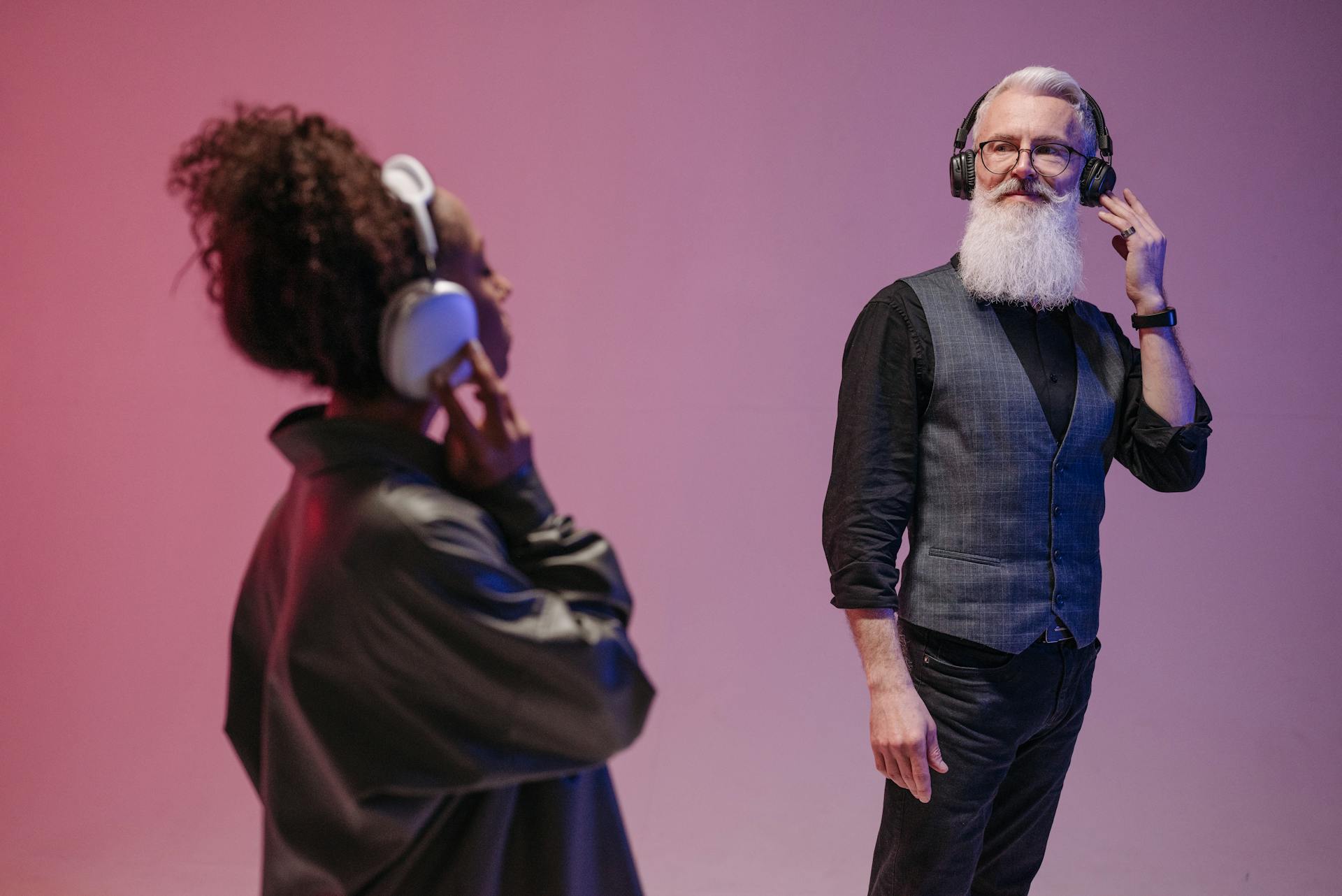 Two people wearing headphones on a pink background