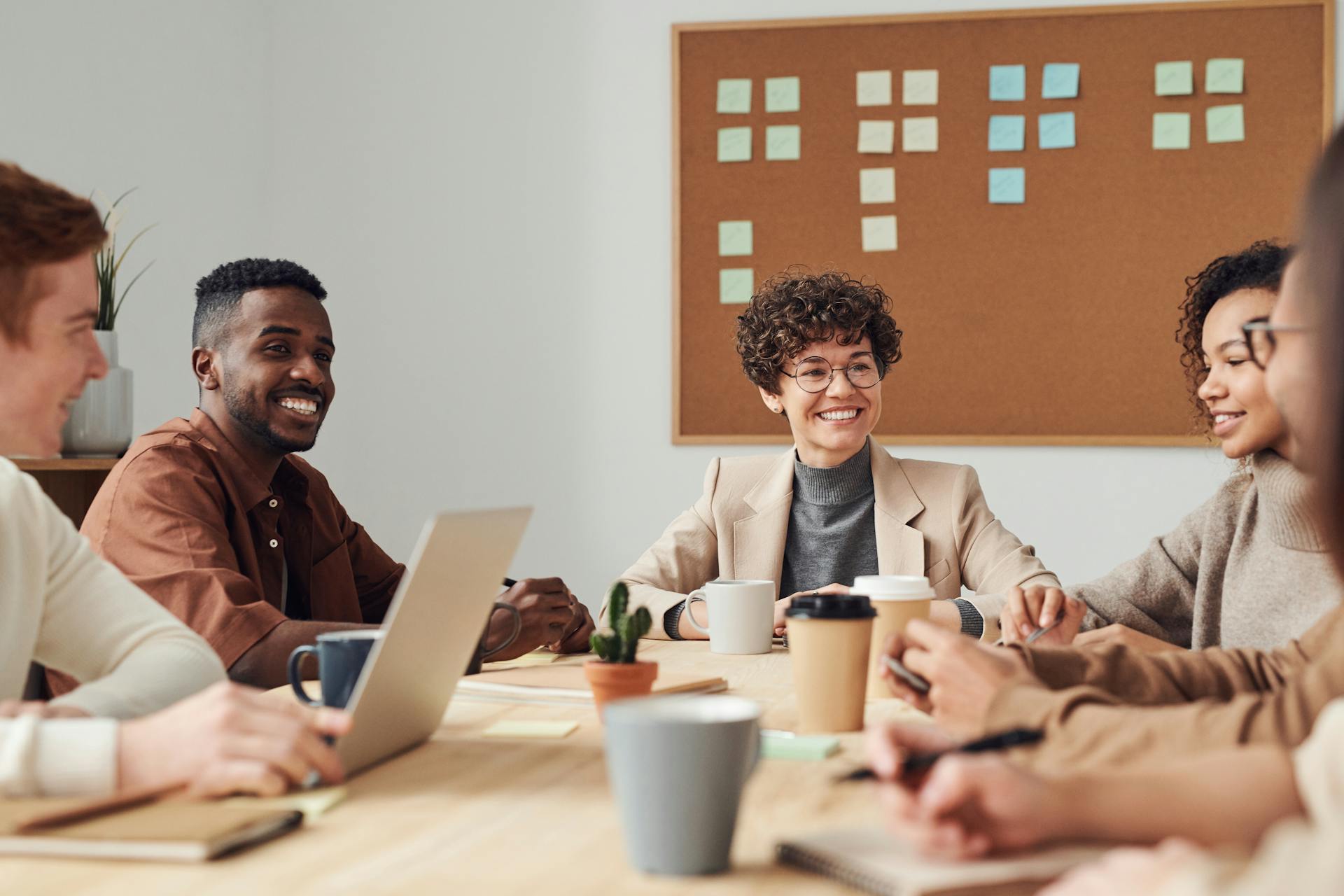 Group of people sitting around a table with a laptop, smiling and engaged in a meeting.