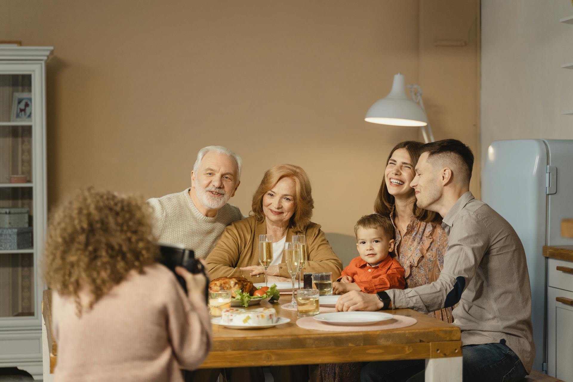 Family of six sitting around a dinner table, with one person taking a photo on a camera.