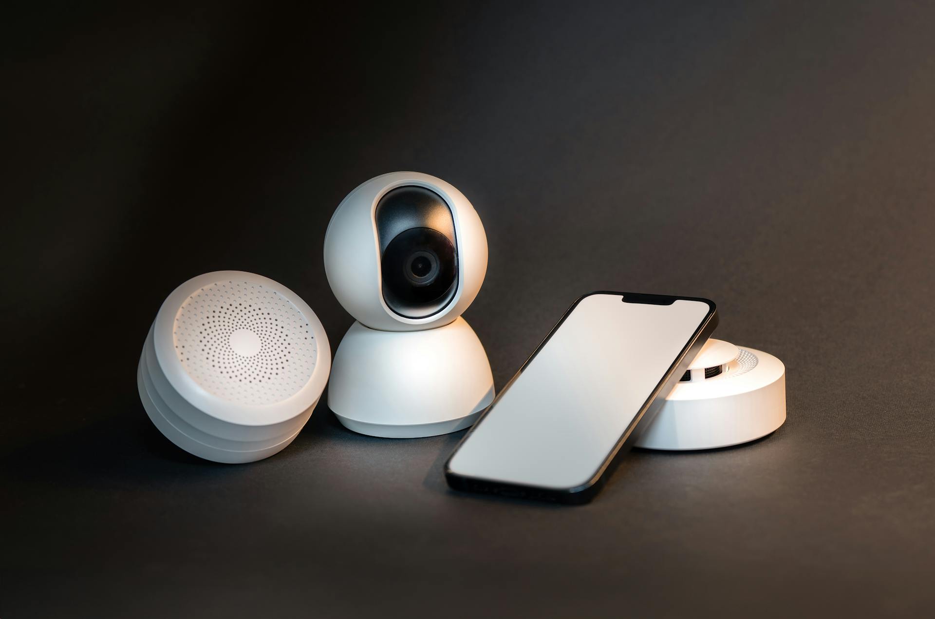 Smart home devices including a camera, speakers, and a phone on a dark background