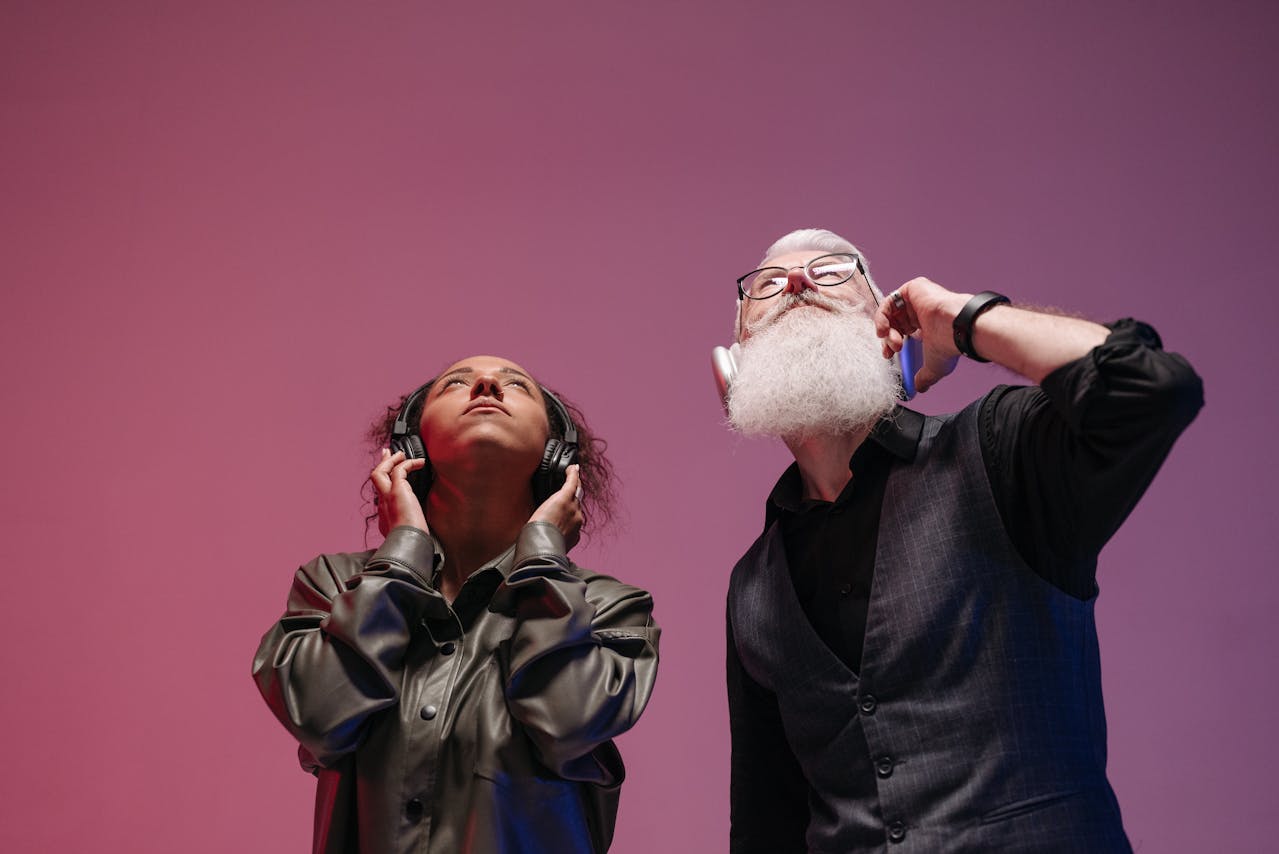 Two people listening to music with headphones against a pink background