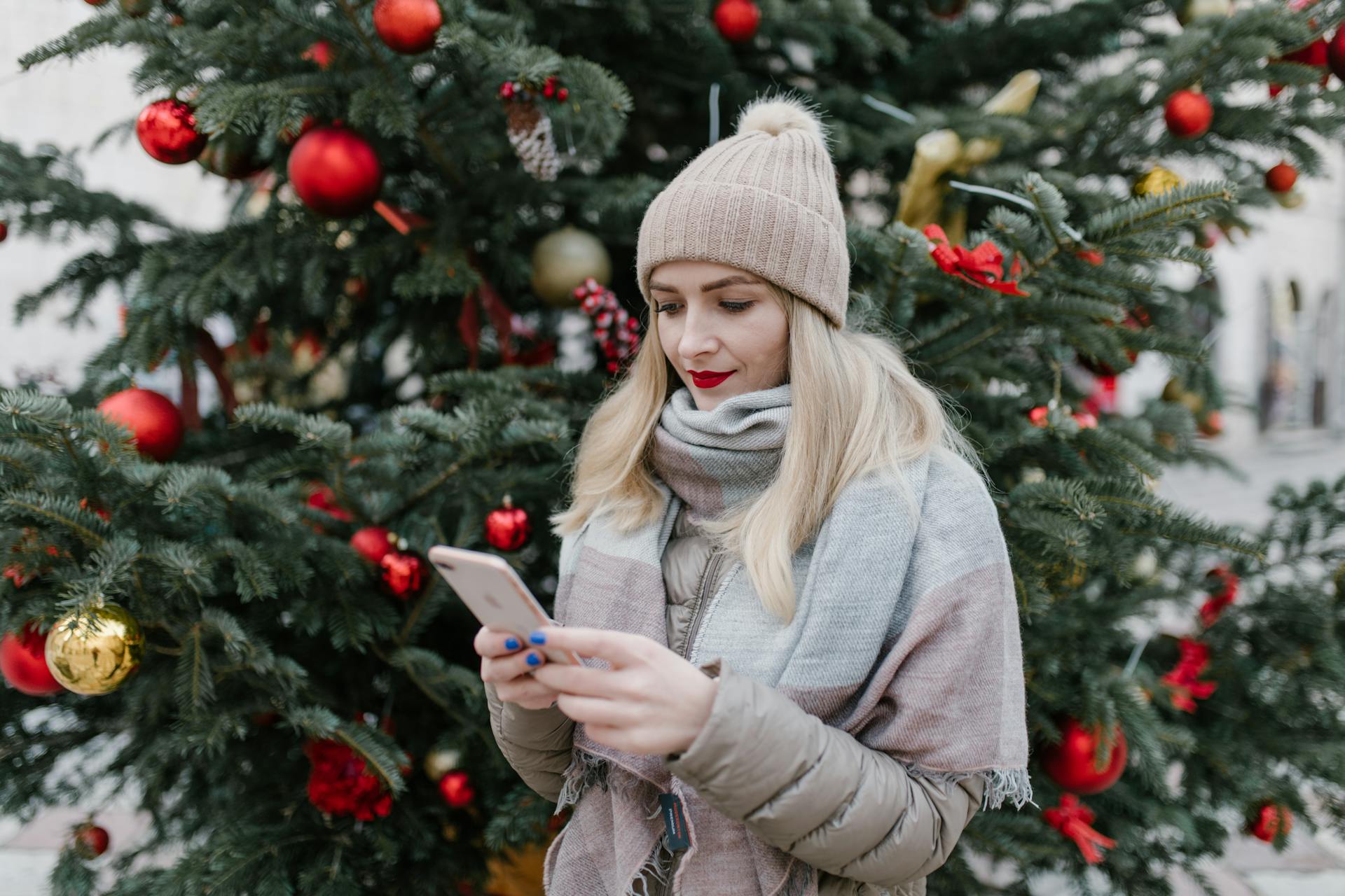 Woman using a phone in front of a decorated Christmas tree