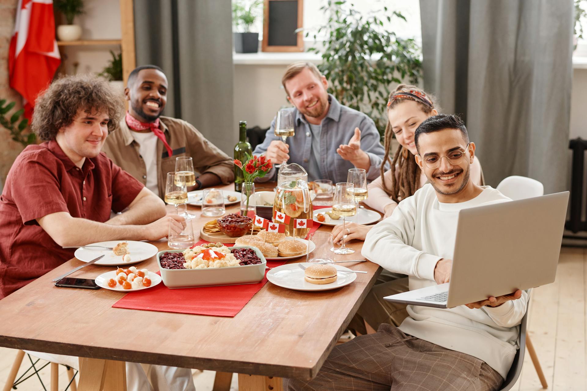 Group of friends gathered around a table for a meal, with one person using a laptop.